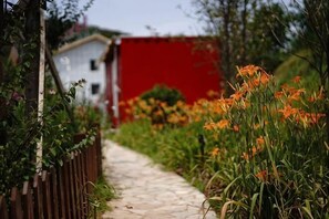A pathway leading to a building with a red facade, surrounded by greenery and orange flowers.
