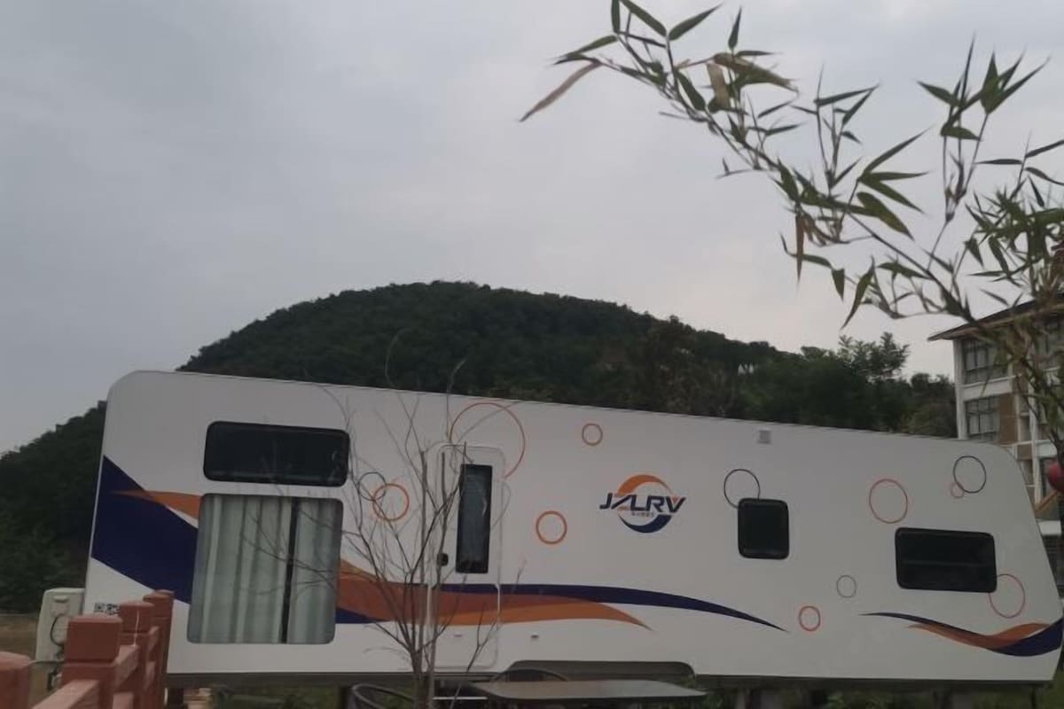 A white RV with a logo and design elements, parked outdoors with a hill in the background.