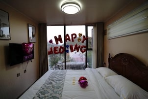 Una camera d'albergo con un letto, una TV a schermo piatto, una finestra con vista e una decorazione con la scritta 'HAPPY WEDDING'.