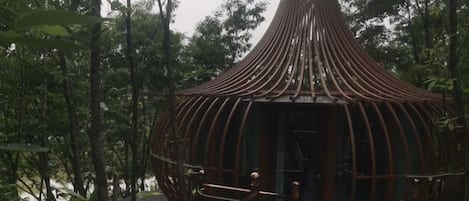 A circular wooden structure with a conical roof, surrounded by dense foliage.