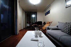 Una stanza con un divano, un tavolino da caffè con tazze e un telecomando, e una porta che dà su un'altra stanza.