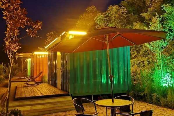 An outdoor patio area with a wooden deck, metal chairs, a round table, and a large umbrella. - Lamangu Resort Hotel (Wugang)