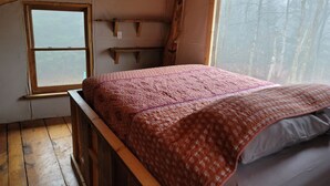 A bedroom with a wooden bed, a window with a view of trees, and a shelf against the wall. - Cabin Retreat in Southern Vermont (Putney)