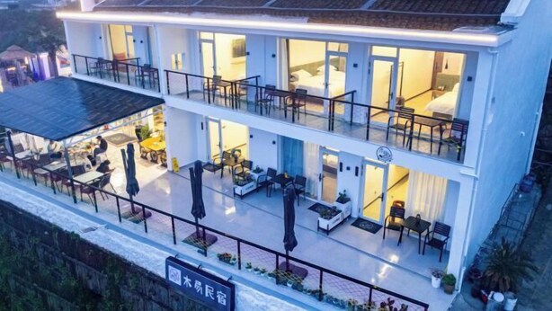 A two-story hotel with a balcony on the upper floor, outdoor seating, and a sign indicating a restaurant. - MU YI (Zhoushan)