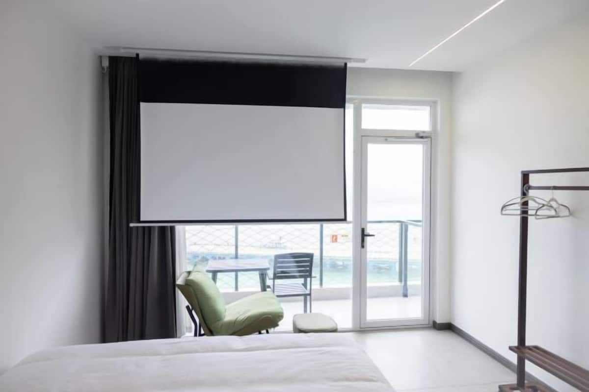 Ein Hotelzimmer mit Bett, einer Sitzecke mit Stühlen, einem Balkon mit Tisch und Stühlen sowie einem großen Fenster.