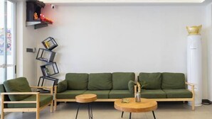 A modern living room with a green sofa, two wooden chairs, and a round coffee table. - MU YI (Zhoushan)