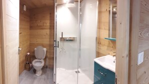 Ein Badezimmer mit Holzwandverkleidung, einer Toilette, einer Duschkabine aus Glas und einem Waschbecken mit Spiegel.