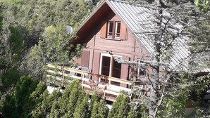 Eine Holzhütte mit geneigtem Dach, umgeben von dichtem Wald und Bergen.
