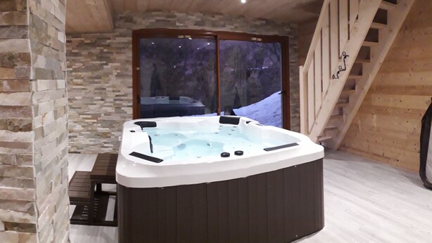 Ein Whirlpool in einem Raum mit Steinwänden, einer Holztreppe und einem großen Fenster.