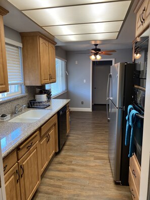 Enjoy cooking in this well-lit kitchen with a refrigerator, oven, and wooden cabinetry.