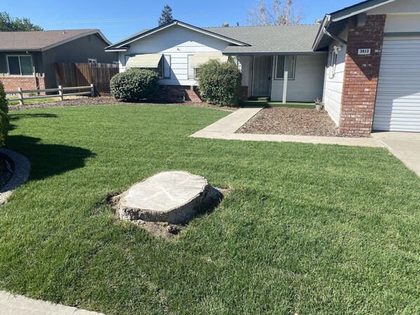 Stunning home with a beautifully manicured lawn and a central stone feature, set behind a brick facade and a wooden fence.