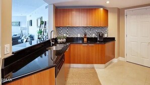 A modern kitchen with wooden cabinets, a black countertop, and a tiled backsplash. - 24TH FLOOR WITH STUNNING ENDLESS VIEWS (Holly Hill)