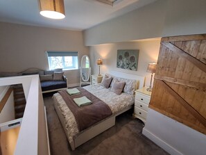 A bedroom with a bed, bedside tables, a mirror, a window, and a wooden wall panel. - Cottage on the Farm (Bassenthwaite)