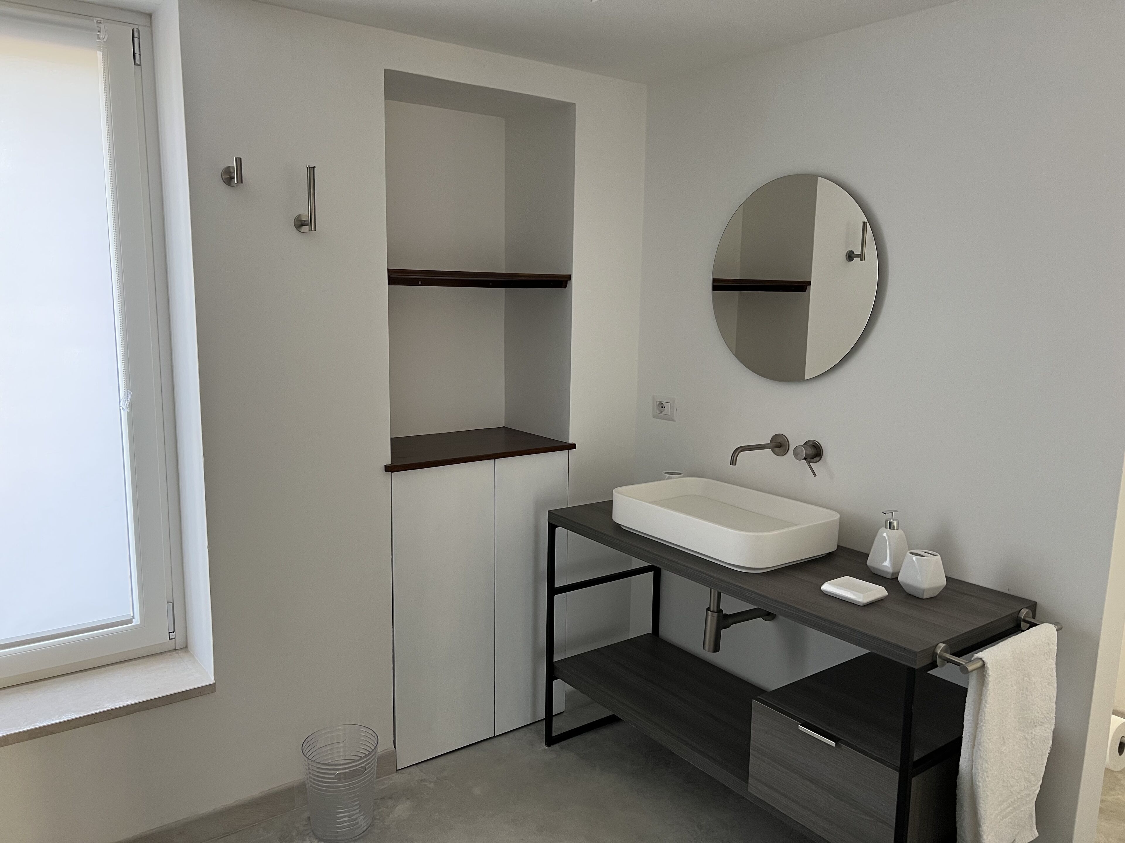 A modern bathroom with a white sink, dark wooden vanity, a round mirror, and a towel hanging on the wall.