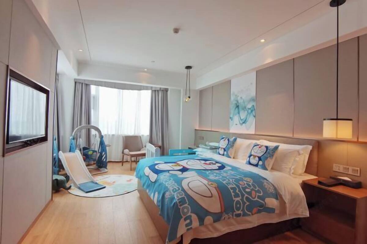 Habitación de hotel con cama, escritorio, silla, ventana con cortinas y una pared decorada con obras de arte.