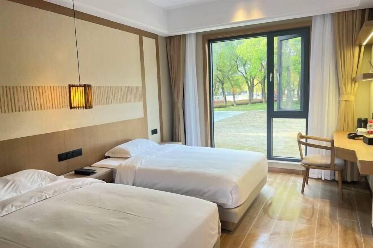 Habitación de hotel con dos camas, un escritorio y vista a un jardín a través de una puerta de vidrio.