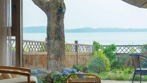 Una habitación con un ventanal grande que da a una masa de agua, una valla de madera y un jardín con diversas plantas.