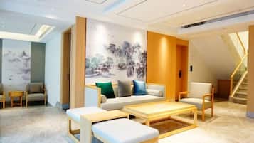 A modern hotel lobby with a sofa, chairs, a coffee table, and a staircase.