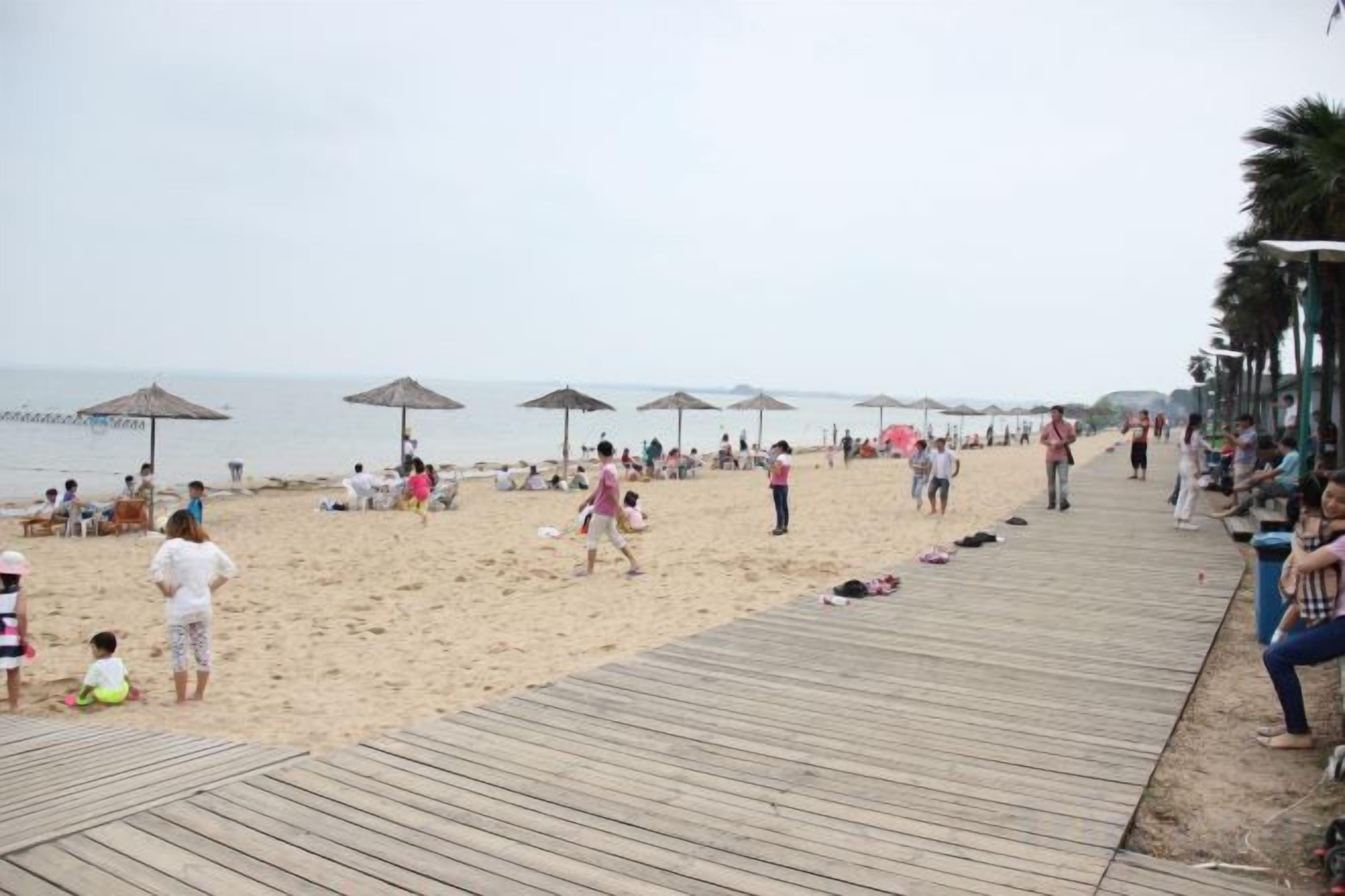 A beach with a wooden boardwalk, umbrellas, and people.