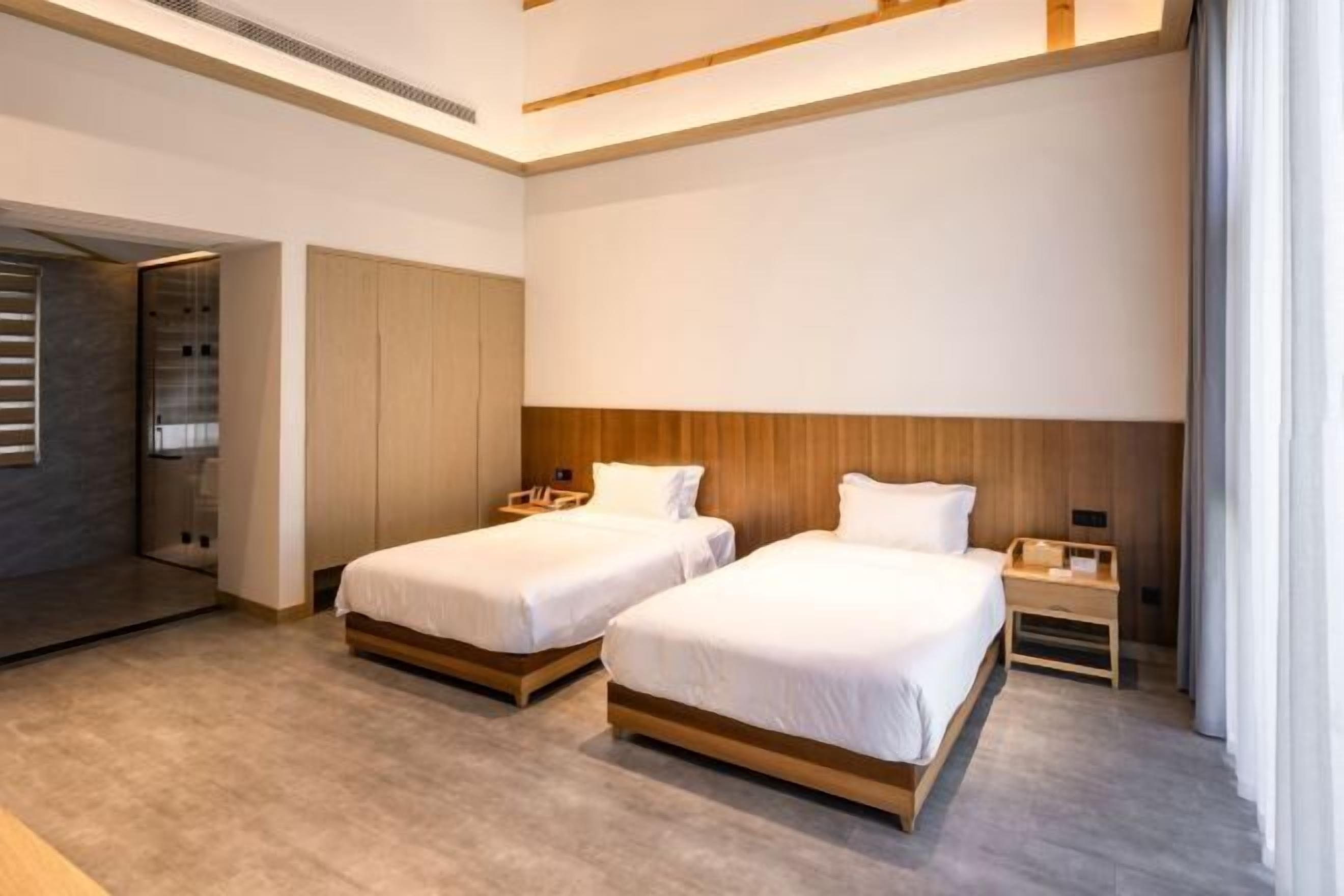 Una habitación de hotel moderna con dos camas individuales, cabeceros de madera y un ventanal con cortinas.
