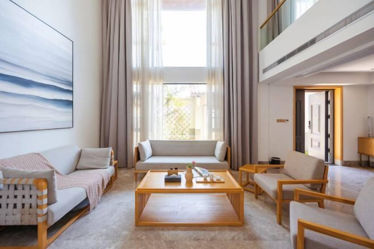 Una sala de estar moderna con un sofá, sillones, una mesa de centro y un ventanal con cortinas.