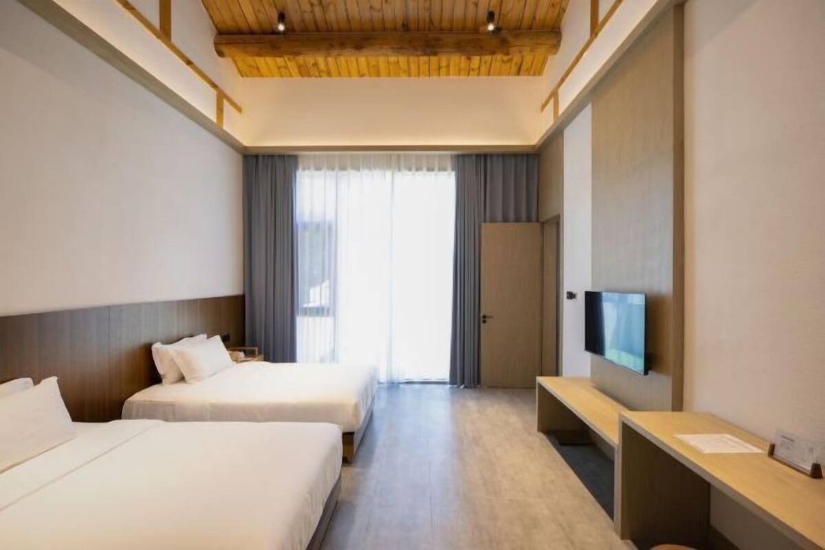 Habitación de hotel con dos camas, un escritorio, televisión y un ventanal grande con cortinas.