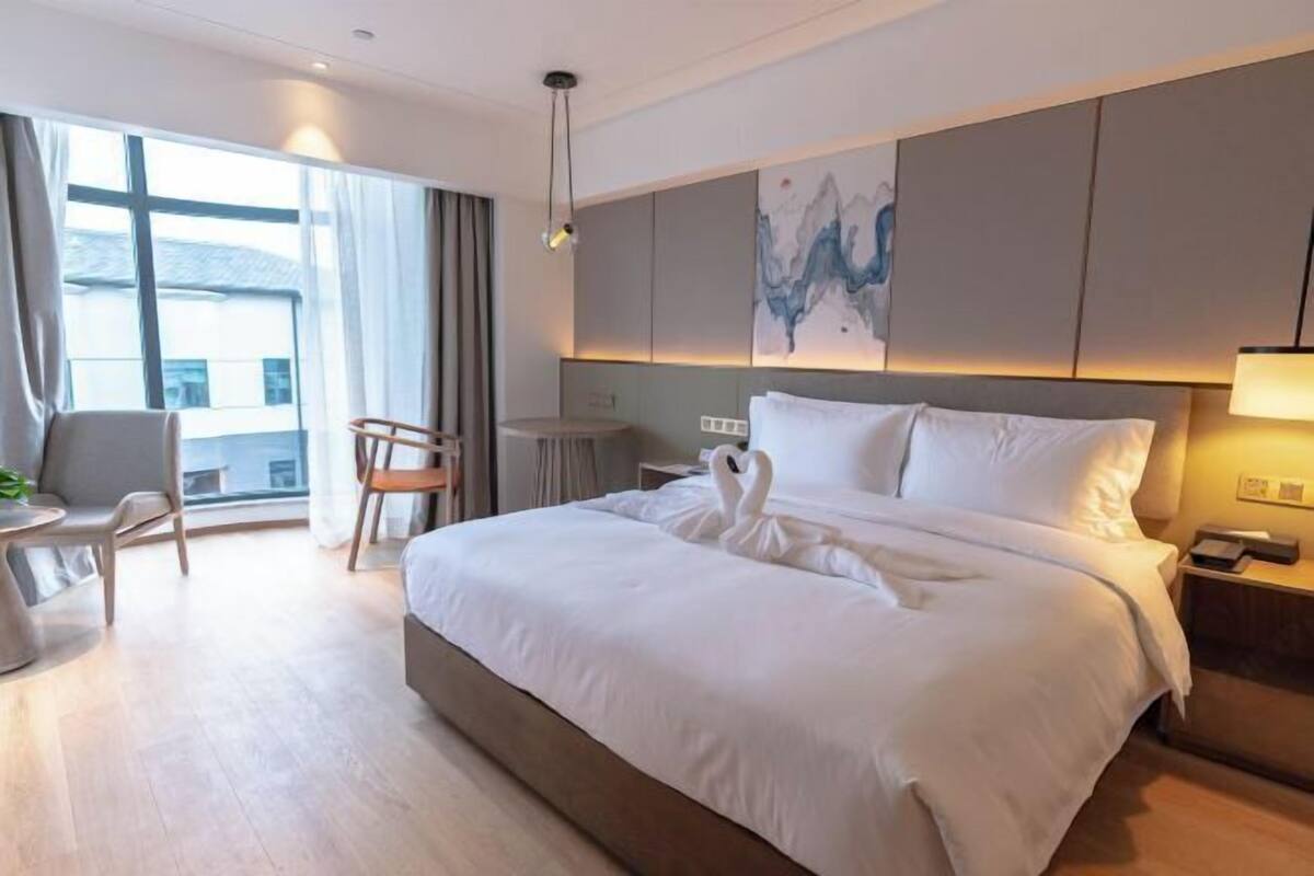 Una habitación de hotel moderna con una cama grande, un escritorio, una silla y vistas al exterior.