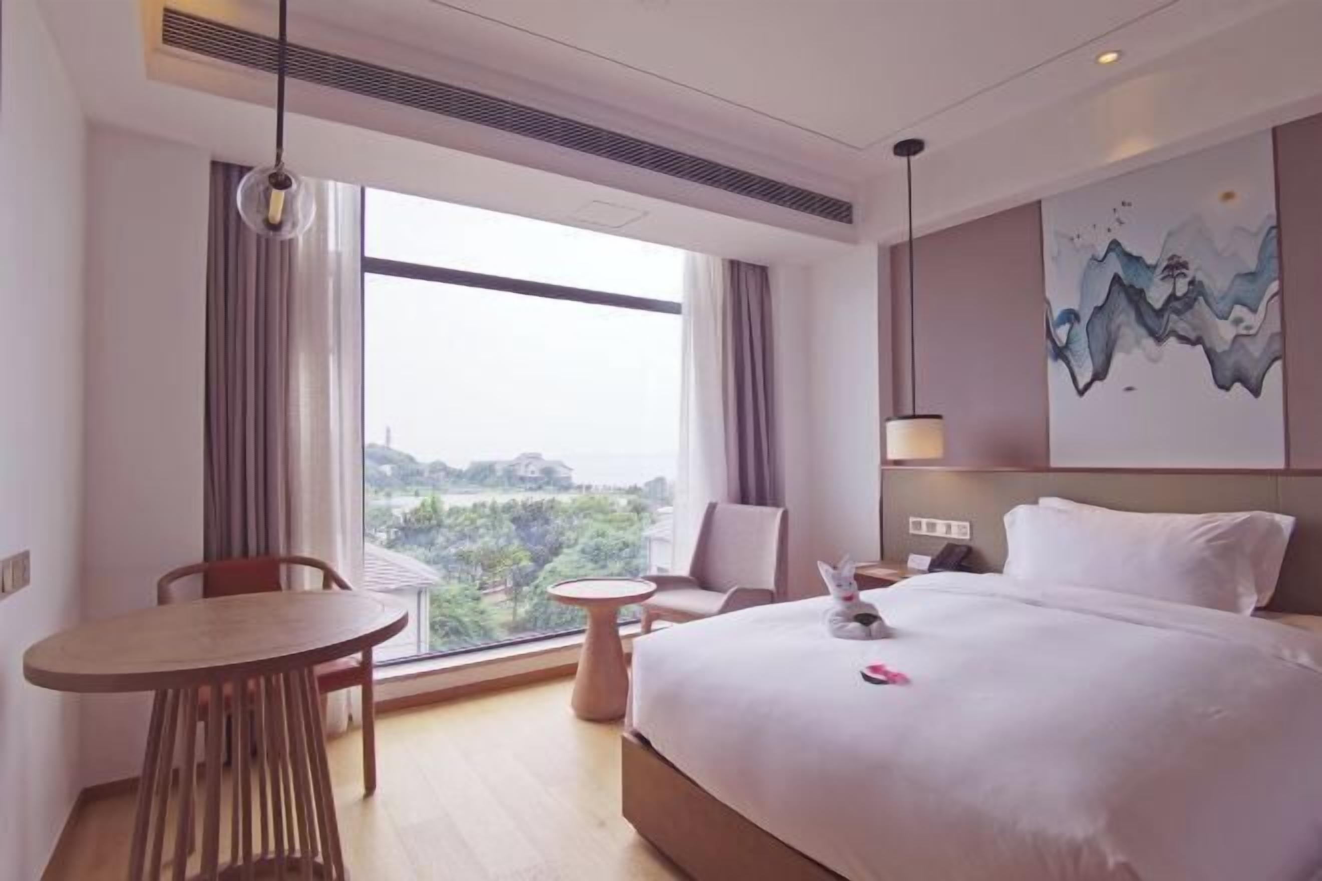 Habitación de hotel con una cama grande, una mesa de comedor, una silla, una pequeña mesa redonda y vistas a zonas verdes por la ventana.