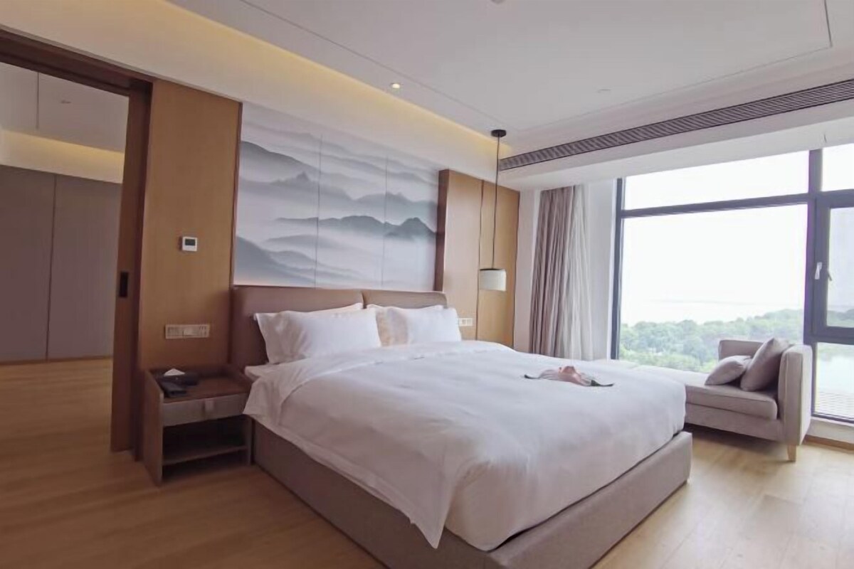 Una habitación de hotel moderna con una cama grande, una mesita de noche, un sofá y un ventanal con vistas.