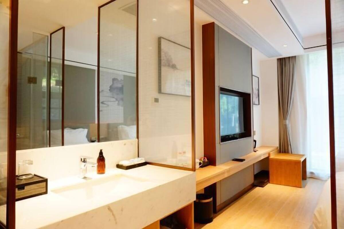 Un baño moderno con un espejo grande, un lavabo, un televisor y un banco de madera.