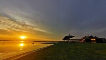 A sunset over a beach with a grassy area and a building with a covered structure.