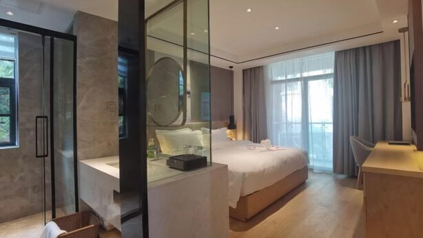 Una habitación de hotel moderna con una cama grande, zona de ducha de vidrio y un escritorio de madera, además de vistas al exterior.