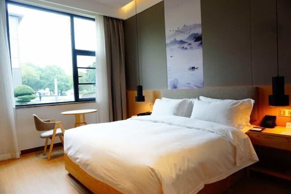 Una habitación de hotel con una cama grande, un escritorio con silla, una ventana con cortinas y una obra de arte colgada en la pared.