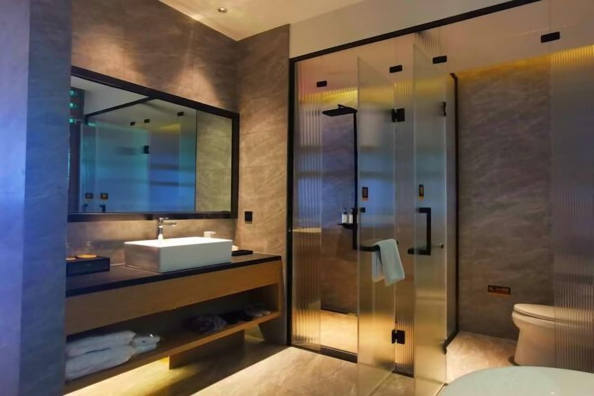Une salle de bain moderne dotée d’une douche à parois de verre, d’un grand miroir et d’un meuble-lavabo avec un évier et un porte-serviettes.
