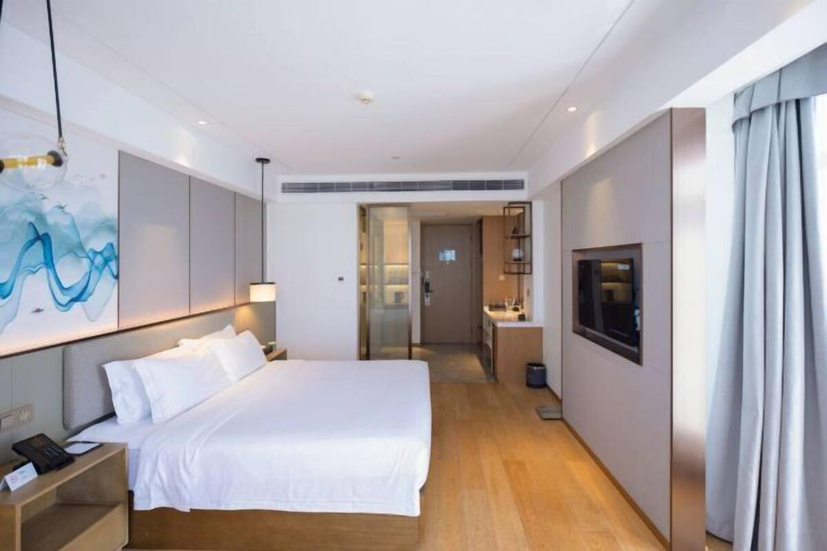 Una habitación de hotel moderna con una cama grande, un televisor, un escritorio y un baño visible a través de una puerta abierta.