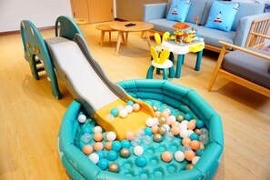 Zona de juegos infantiles con tobogán, piscina de pelotas y una pequeña mesa con juguetes.