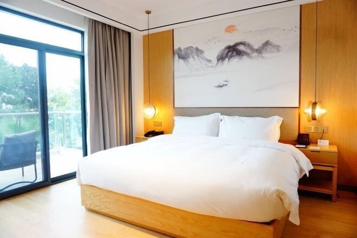 Una habitación de hotel moderna con una cama grande, cabecera de madera y un cuadro de montañas en la pared.
