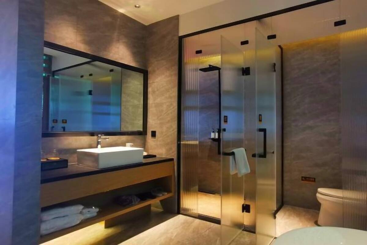 Un baño moderno con ducha de vidrio, un espejo grande y un tocador con lavamanos y perchero para toallas.