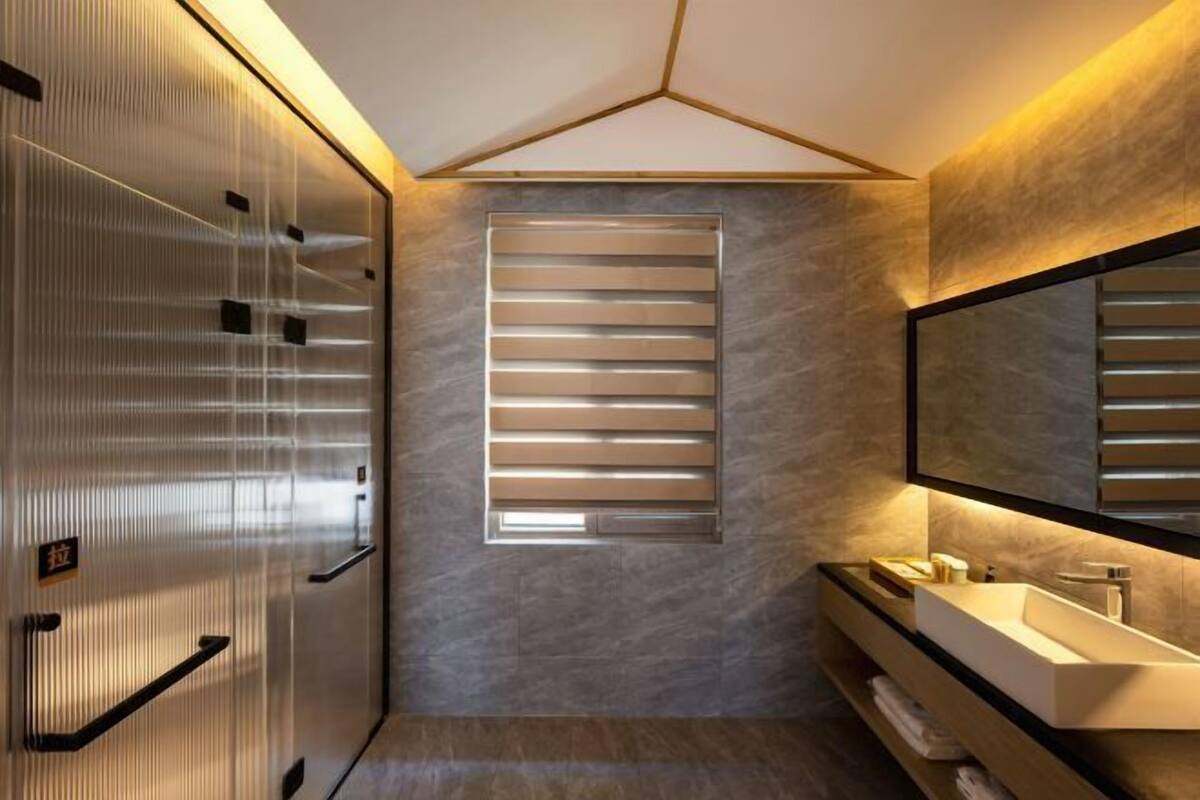 Un baño moderno con un espejo grande, un lavamanos empotrado y un ventanal con persianas horizontales.