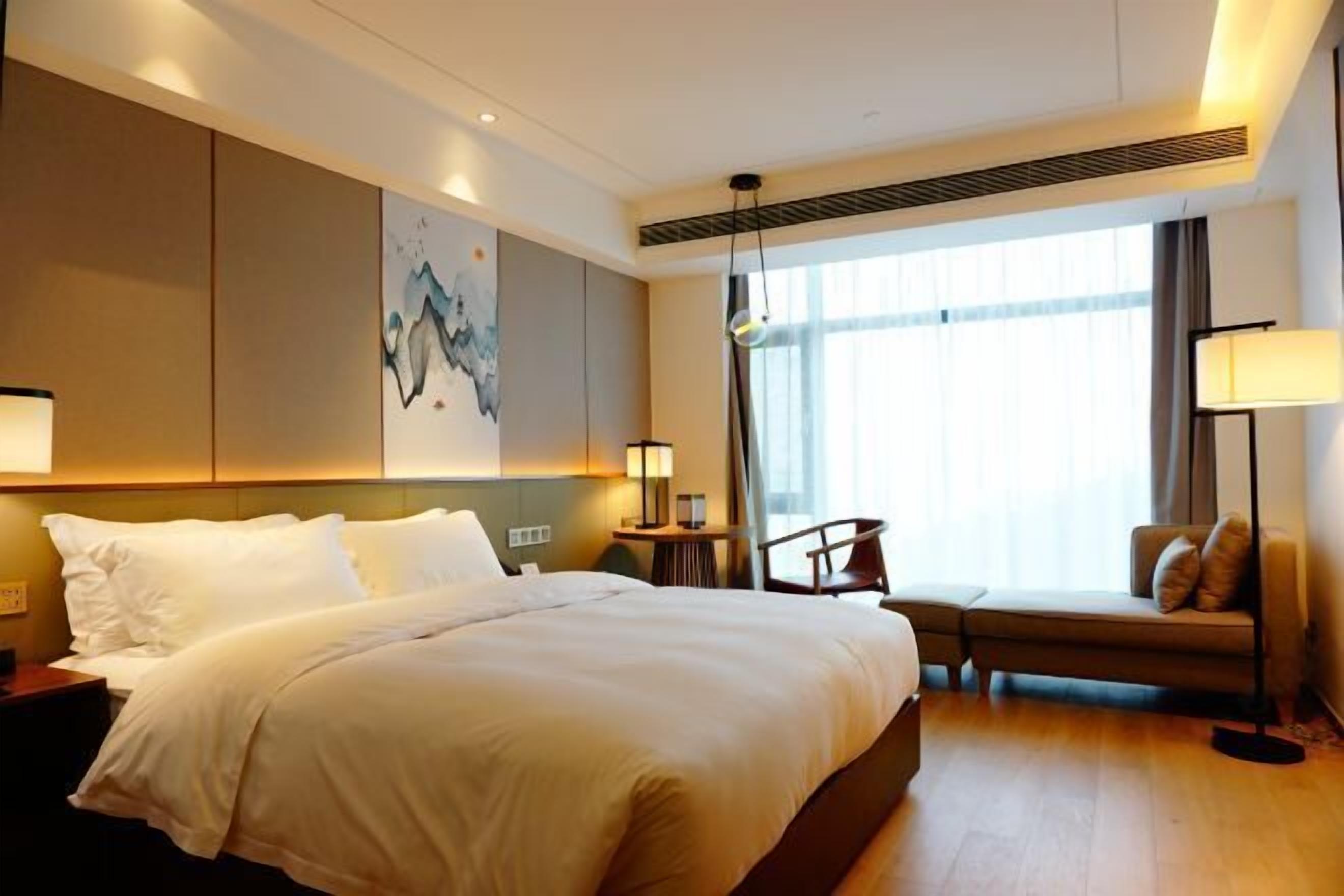 Habitación de hotel con una cama grande, un escritorio, una silla, un sofá y un ventanal con cortinas.