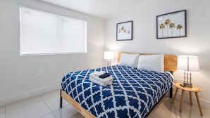 A neatly made bed with a patterned bedspread, a bedside lamp, and two framed pictures on the wall. - Miami Suite 308 (Miami)