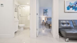A modern bathroom with a toilet and shower, a bedroom with a bed and a nightstand, and a living area with a leather sofa. - Miami Suite 308 (Miami)