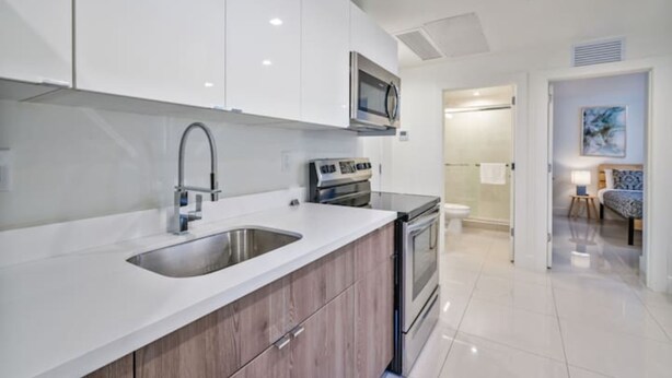A modern kitchen with white cabinets, stainless steel appliances, and a double sink. - Miami Suite 308 (Miami)