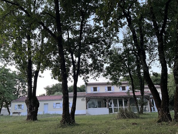 Un edificio de dos plantas con techo de tejas rojas, rodeado de árboles y césped.