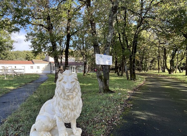A white lion statue in a park with trees and a building in the background. - Villa de L Eguille (L'Eguille)