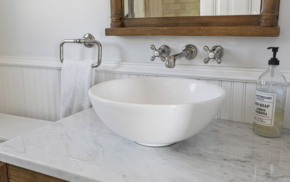 A white ceramic basin on a marble countertop, a wooden-framed mirror above, and a bottle of liquid soap to the right. - Beautiful upper level 2b/2b flat in 1885 Queen Anne Cottage in Alameda (Alameda)