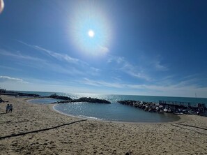 A beach with a clear sky, a rocky breakwater, and a wooden pier.