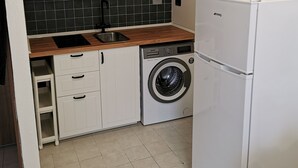 Una cocina compacta con muebles blancos, lavadora y refrigerador.
