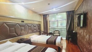 Ein Hotelzimmer mit zwei Betten, einem großen Fenster mit Vorhängen, einem Sessel, einem kleinen Tisch und einem an der Wand befestigten Fernseher.