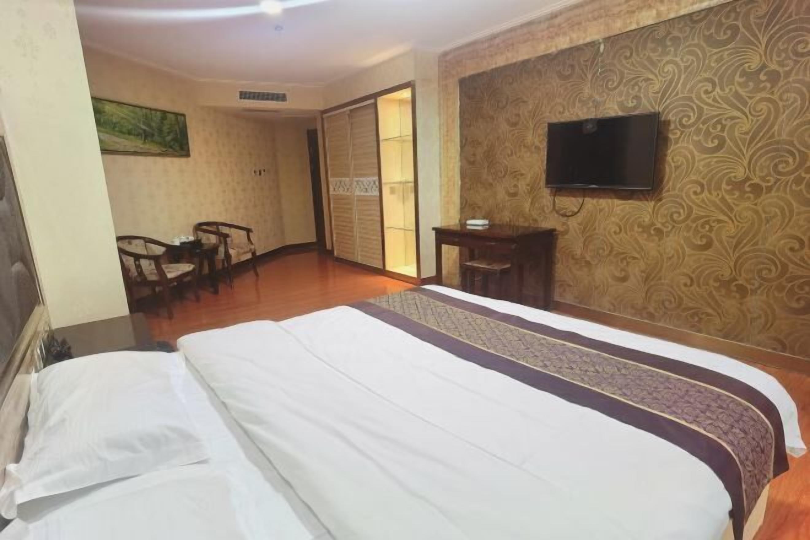 A hotel room with a bed, a desk, a chair, a television, and a wardrobe.